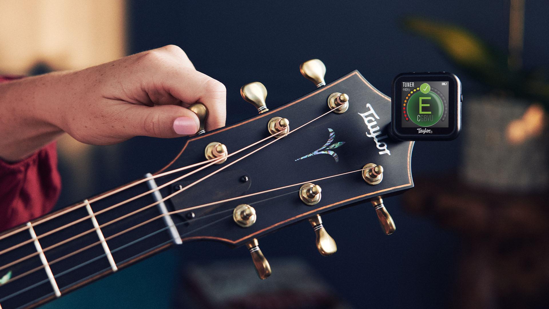 An image of a woman tuning her guitar. There is a tuner attached to the pegboard, and she is turning one of the pegs.